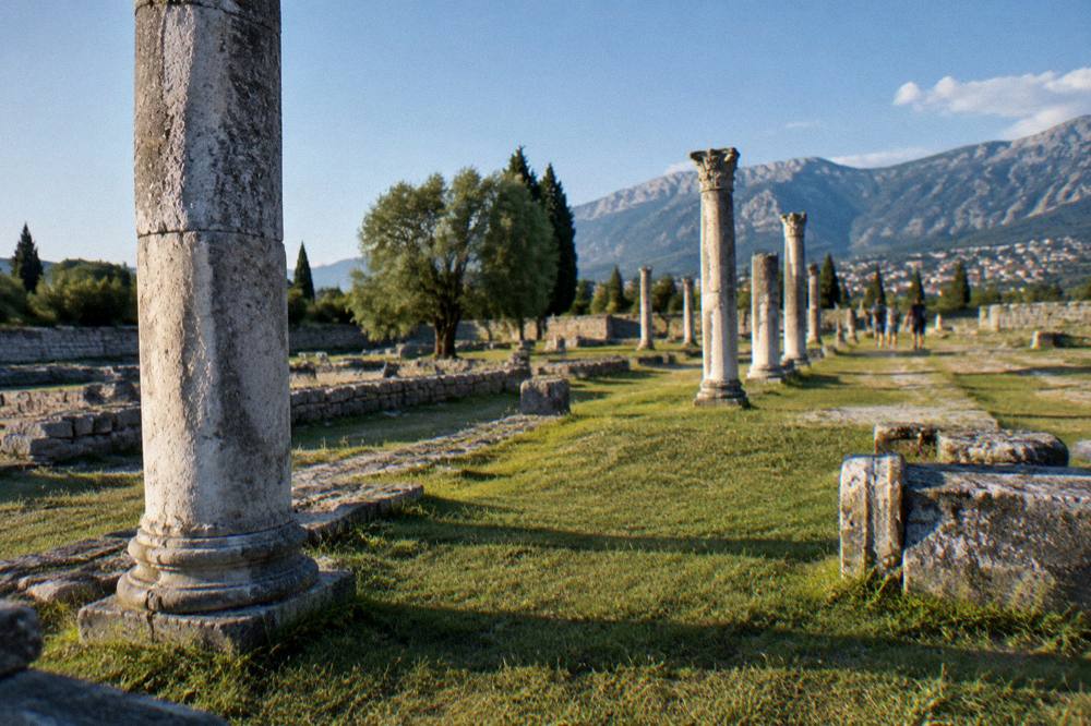 Stone ruins of the Roman town of Salona with columns and grass under a blue sky
