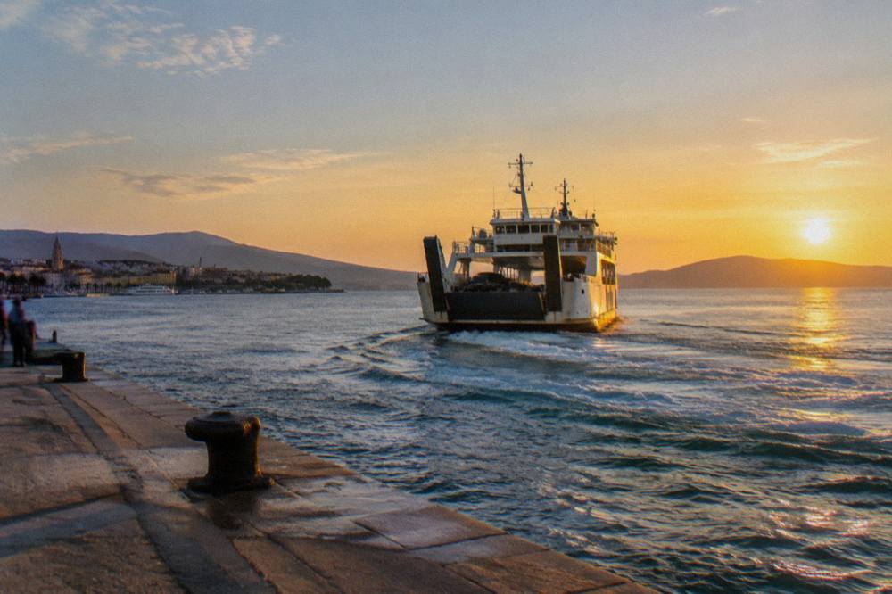 A car ferry leaving Split port with islands on the horizon at golden hour