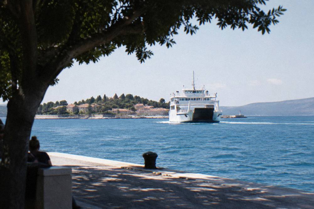 A white car ferry approaching an island port across blue Adriatic water