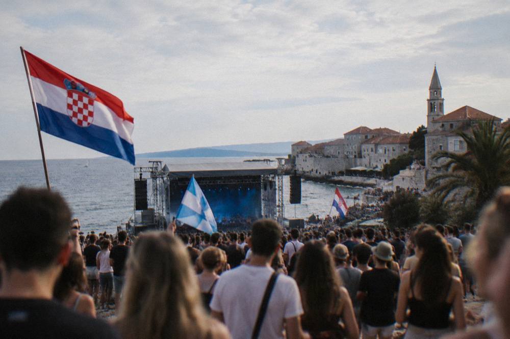 A crowd with flags at an outdoor music festival ground near the sea