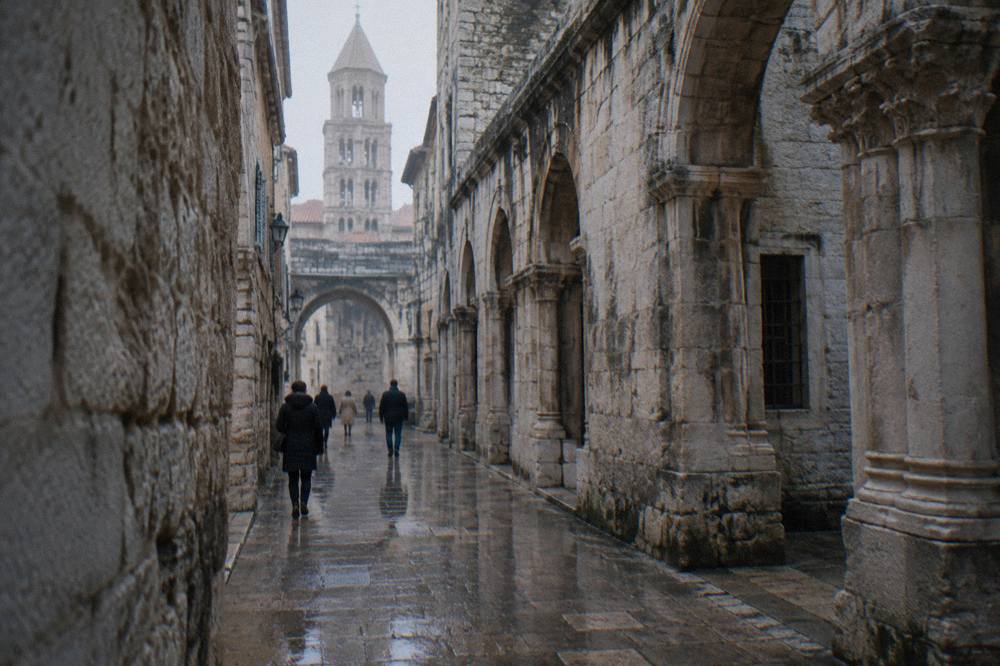 Rain-darkened stone alley inside Diocletian's Palace in Split with a few people in coats walking