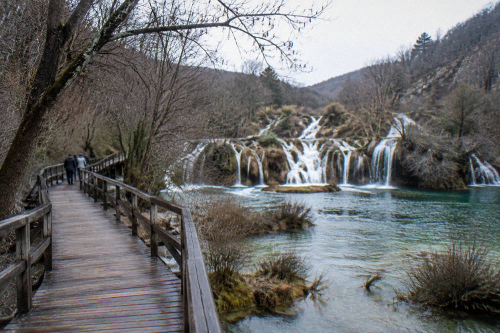 Wooden waterfalls walkway at Krka National Park in winter with bare trees and low water
