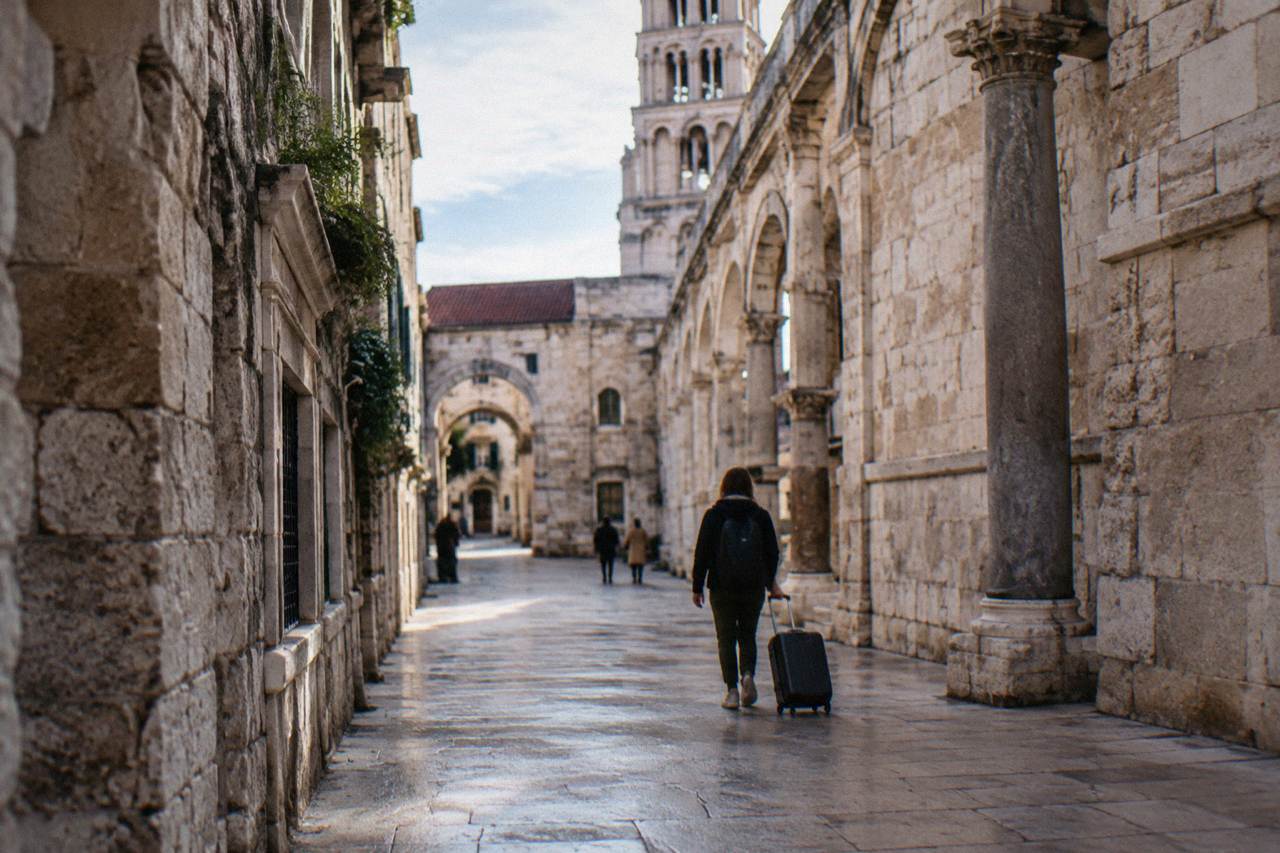 A stone street inside Diocletian's Palace in Split with a traveller rolling a suitcase over smooth paving