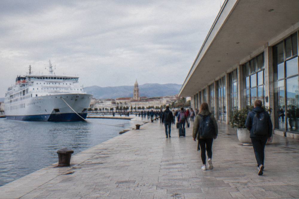Travellers with backpacks walking beside the ferry terminal building on the Split waterfront