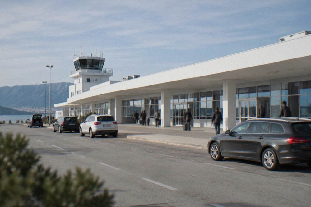 The white terminal building of Split Airport under a clear sky with cars at the kerb