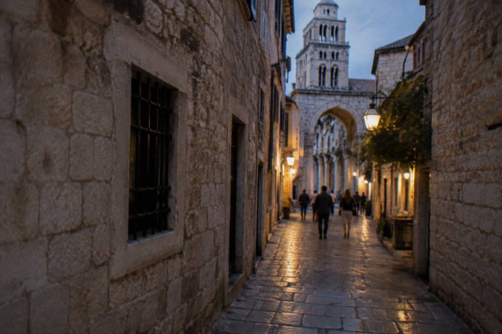 Lit stone alley inside an old Mediterranean town at night with people walking