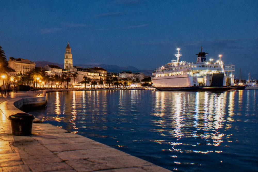 Harbour at night with a lit ferry and promenade lights reflecting on the water