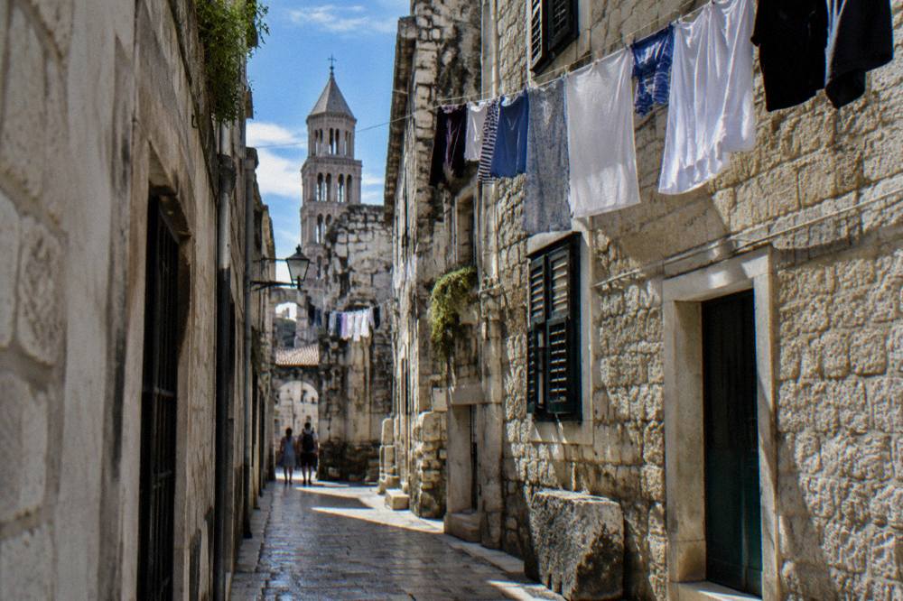 A narrow stone street inside a Roman palace quarter with laundry hanging above