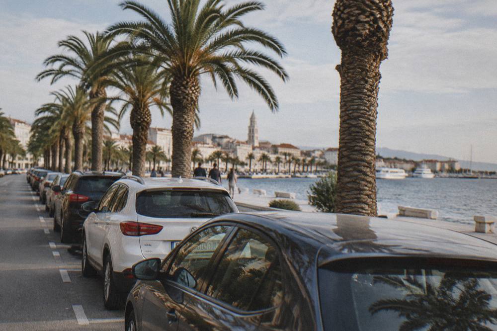 A line of cars parked along a palm-lined street beside the seafront promenade in Split