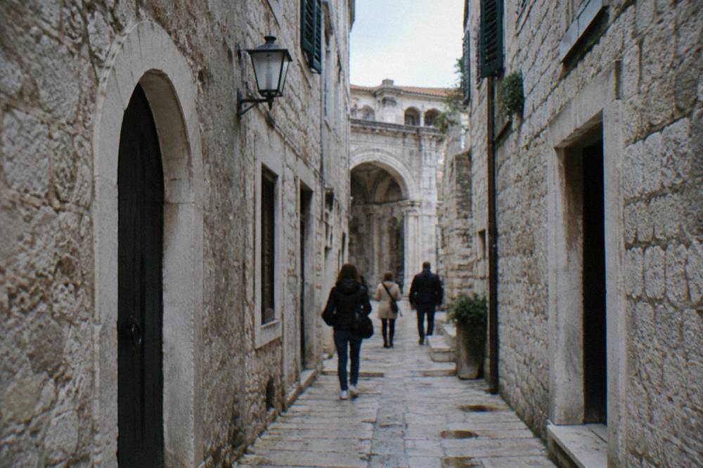 People walking through a narrow stone lane inside the old quarter of Split