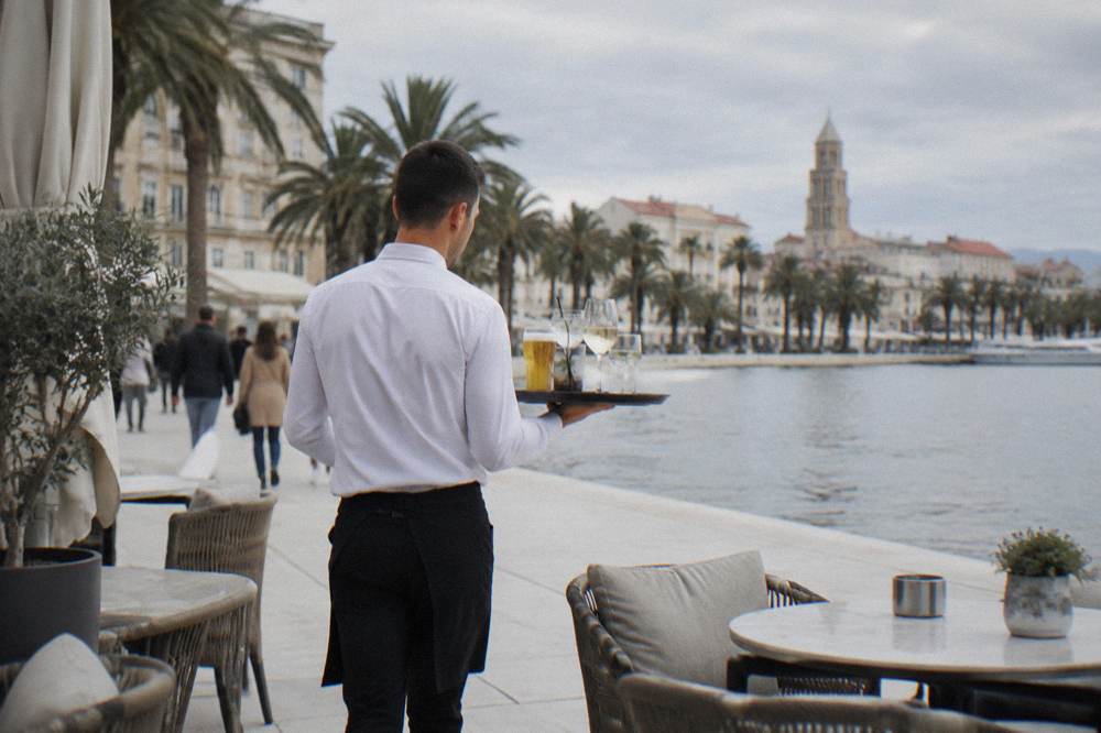 A waiter carrying a tray of drinks to a terrace table in Split