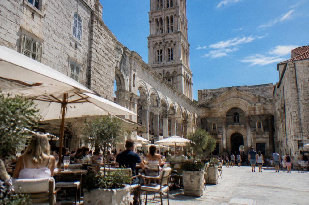 People dining at outdoor tables on a sunny square in Split