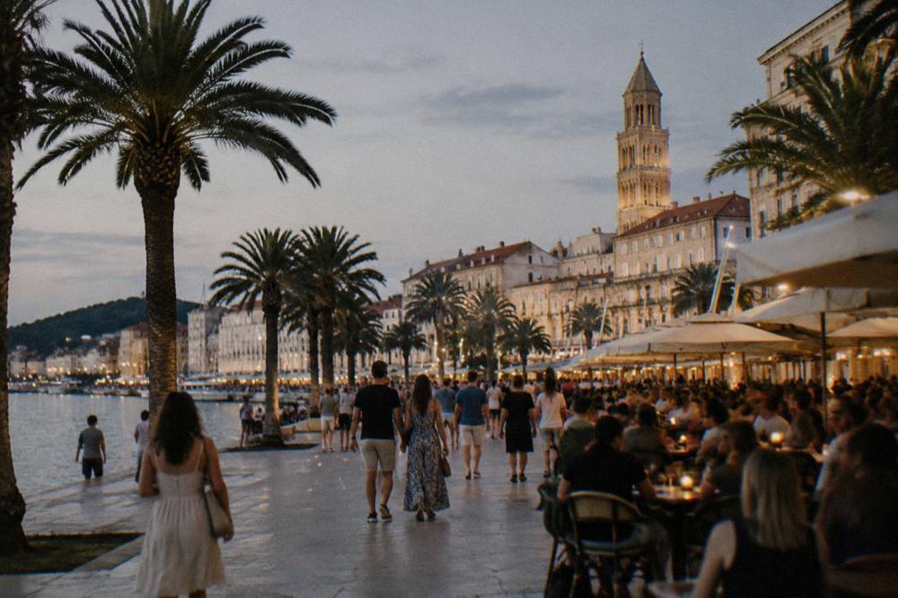 Crowds and café lights in a stone square in Split at night