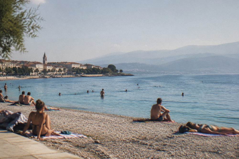Sunbathers and swimmers at a pebble beach near Split with calm blue sea