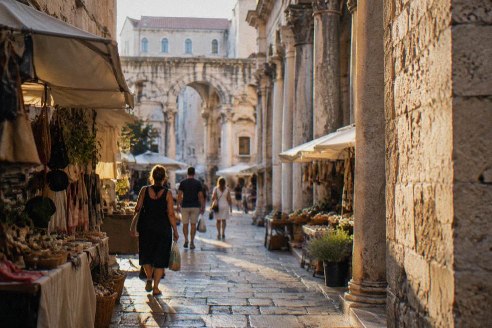 Shaded market street in Split in the morning with shoppers carrying bags