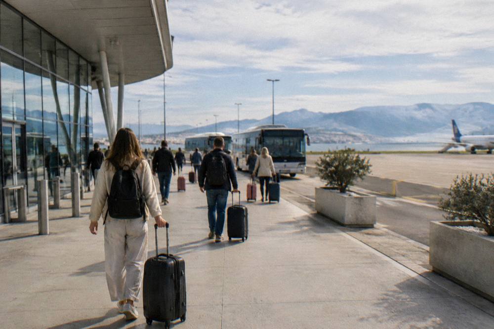 Passengers with luggage walking out of Split Airport terminal towards buses
