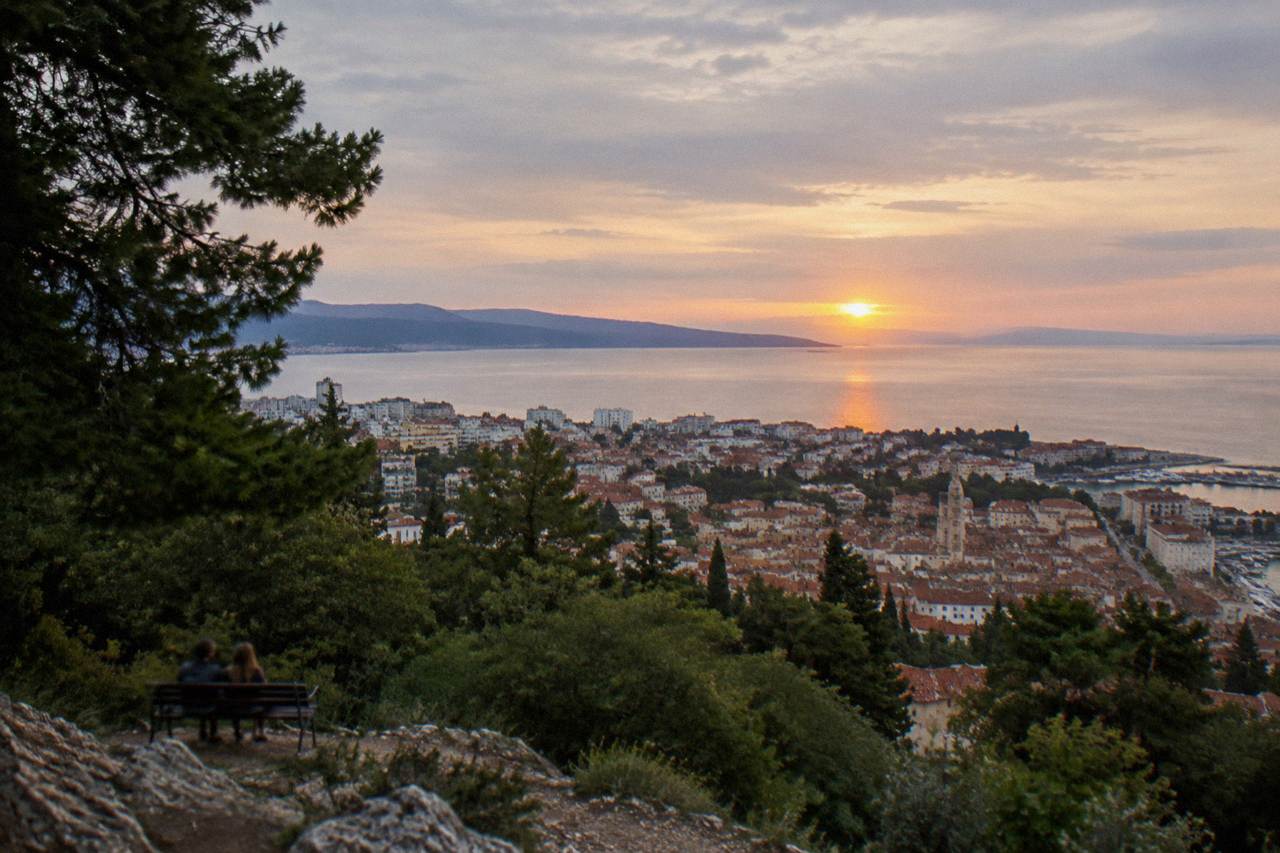 The sun setting over the Adriatic Sea as seen from a wooded hill above the rooftops of Split