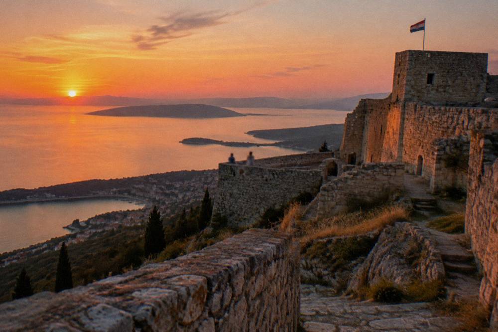 A stone fortress on a ridge above the coastline glowing in low evening light