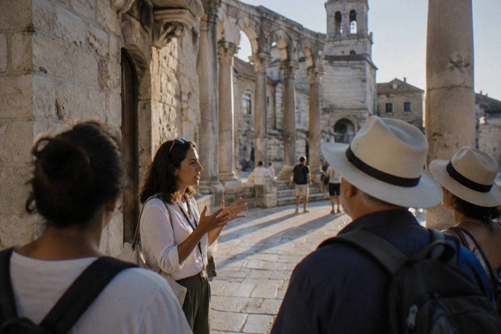 A guide speaking to a small group of visitors on a stone street in an old Mediterranean town