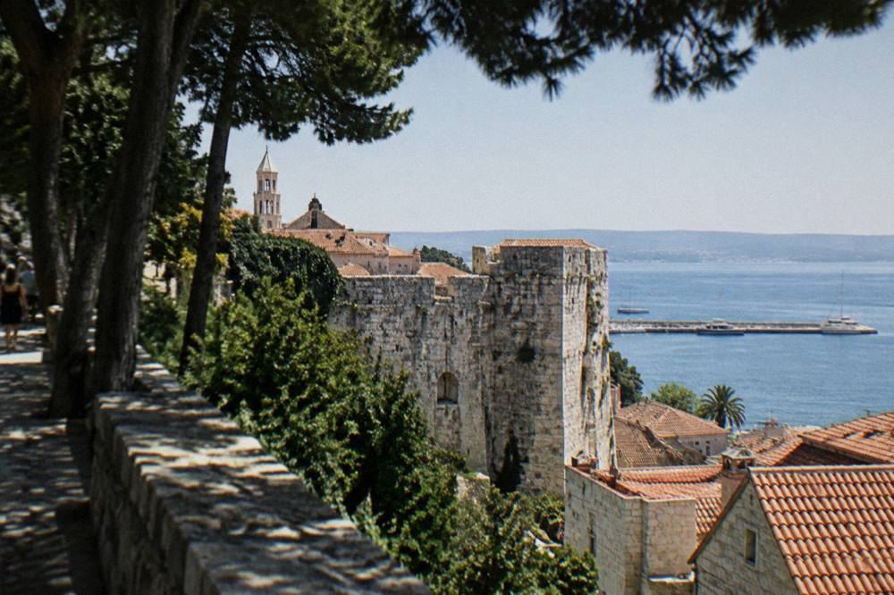 A stone fortification wall rising above terracotta rooftops beside a calm blue sea