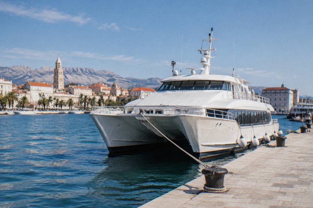 A white catamaran fast boat moored at a stone quay in a small Dalmatian harbour