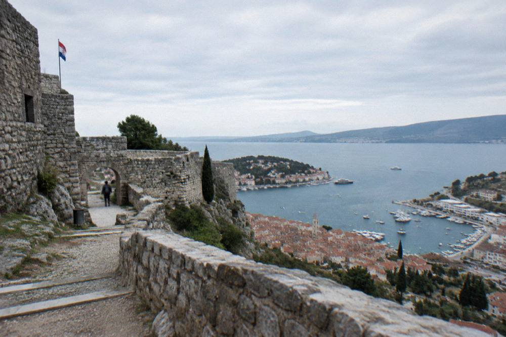 A hillside fortress overlooking a red-roofed island town and a bay with yachts