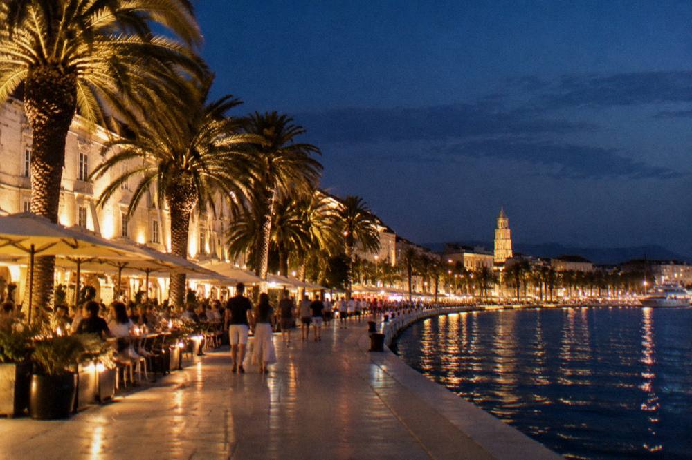 The illuminated Riva promenade in Split at night with cafe terraces and palm trees along the water