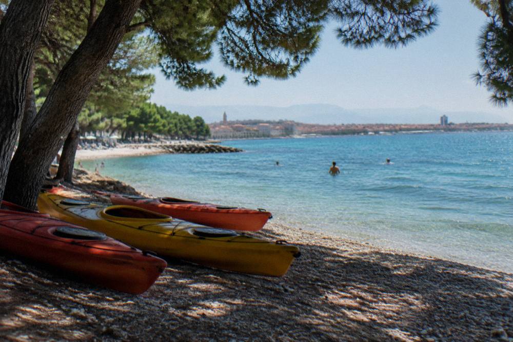 Kayaks resting on a small pebble beach below pine trees near the Split coastline