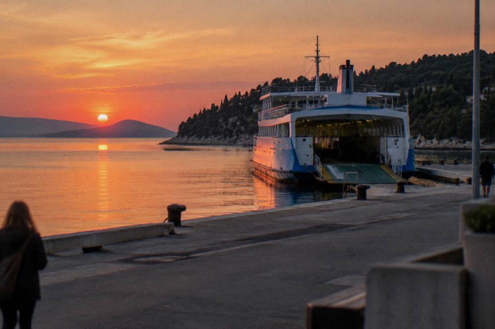 Ferry port at dusk with an island ferry docked and a forested peninsula behind