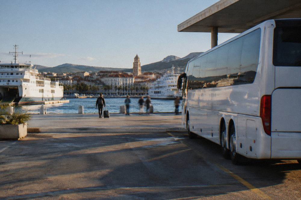 A long-distance coach parked at a bus station beside ferries moored at a waterfront