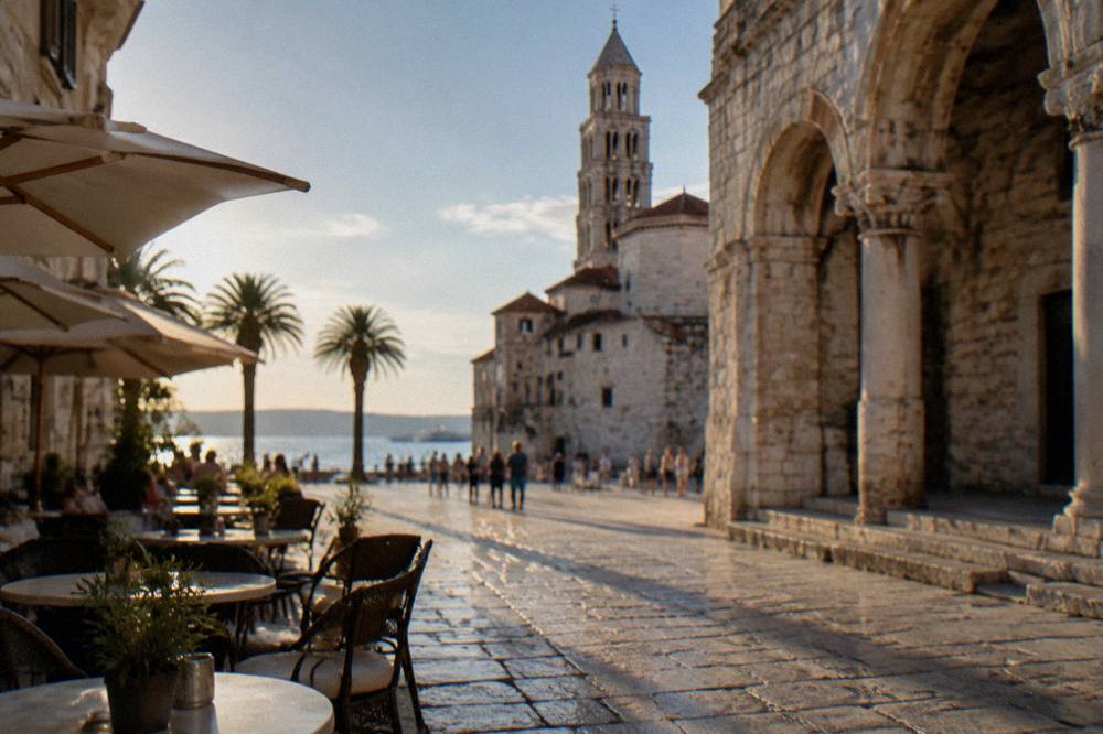 A seaside square with historic stone buildings and cafe tables in Split