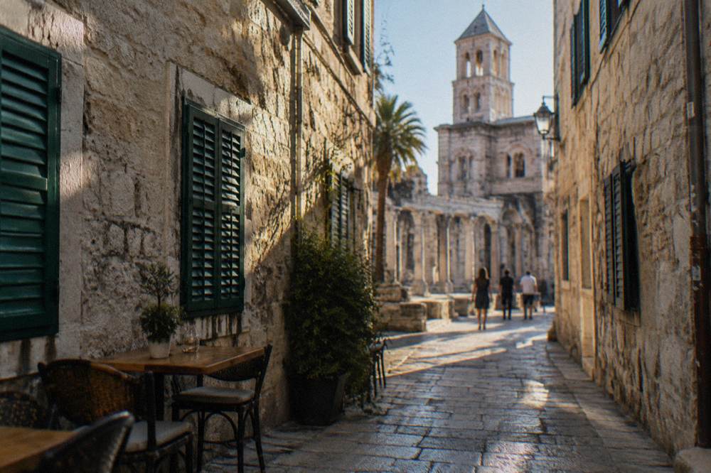 Stone alleyway in a Dalmatian old town with shutters and a cafe table