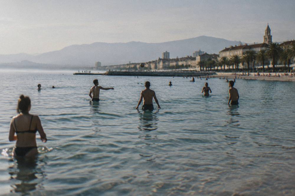 People playing picigin in shallow water at a sandy city beach