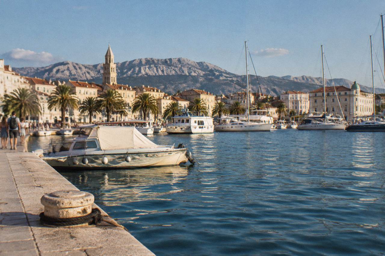 Boats moored in a harbour with stone buildings and hills behind them