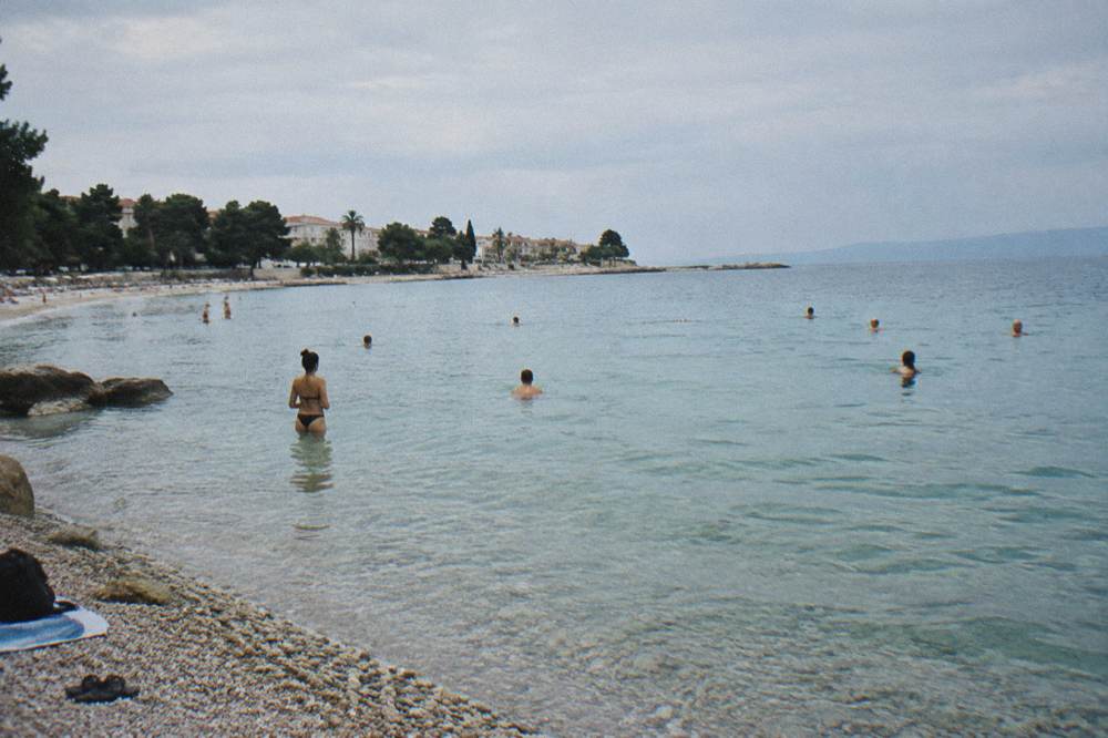 People swimming on a pebble beach beside clear shallow water
