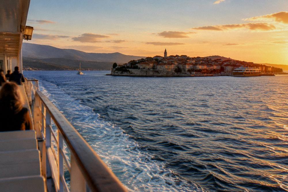 A ferry crossing blue water toward an island town in the distance