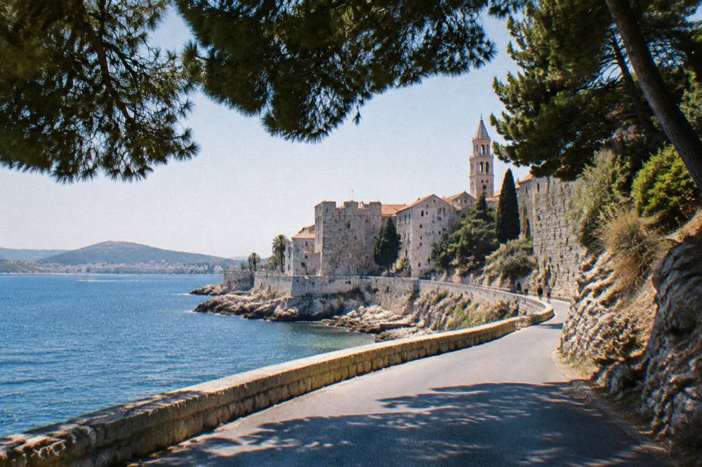 A coastal road curving along the Adriatic shoreline with dry stone hills and pine trees
