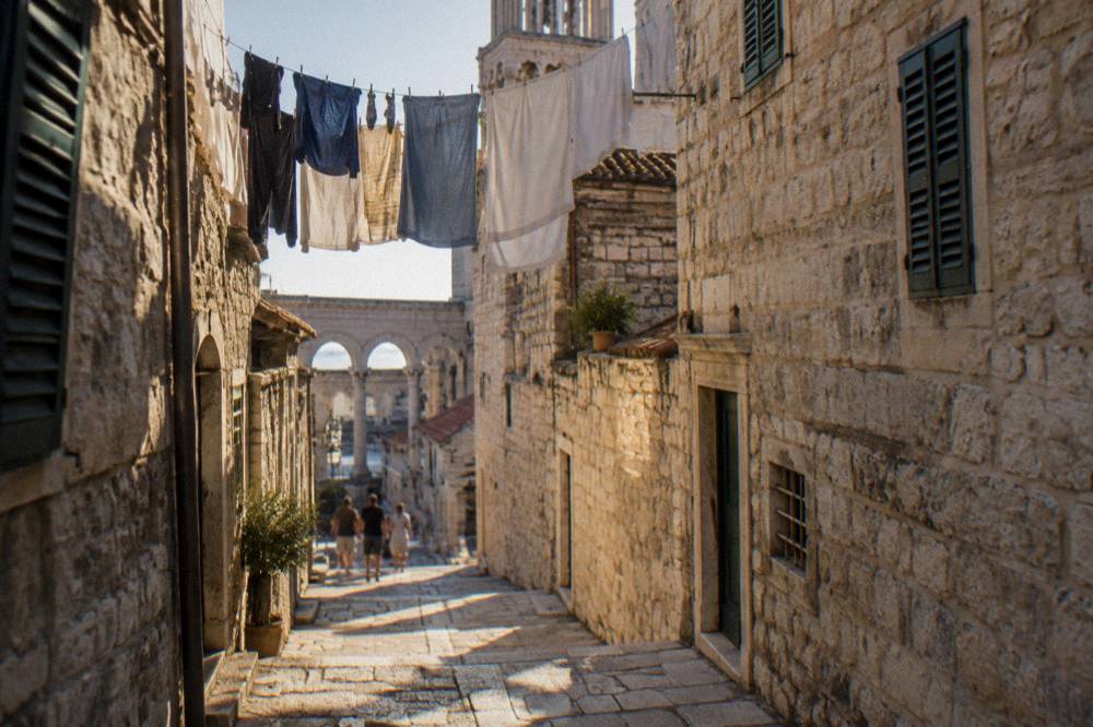 A stone street in an old Dalmatian town with laundry hanging above and sunlight on worn steps