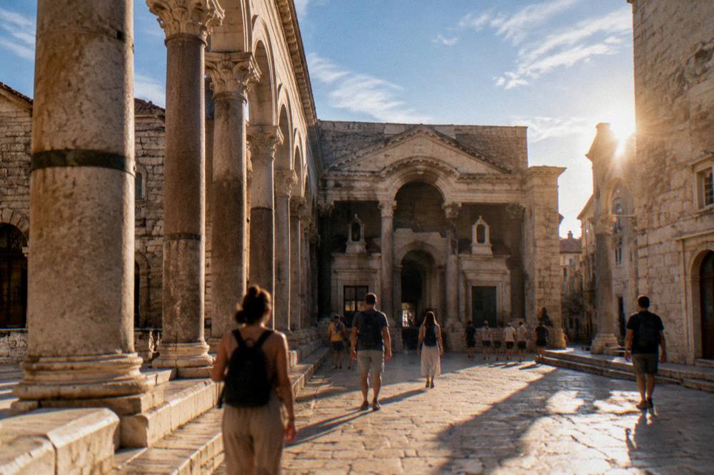 Visitors with daypacks walking past Roman columns in Split at golden hour
