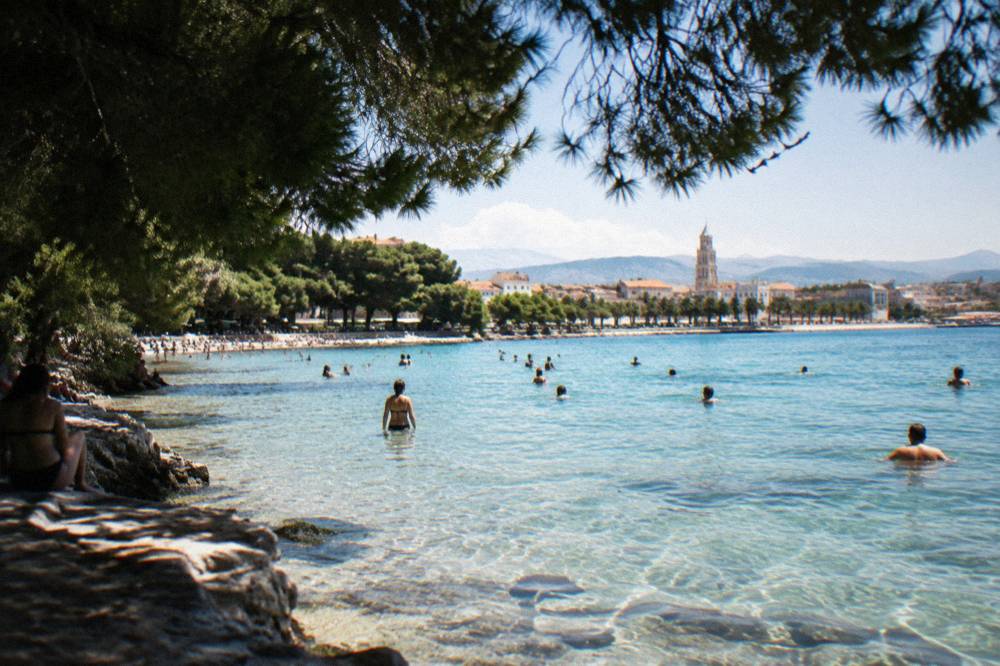 People swimming in the clear shallow water at a city beach in Split on a bright summer day