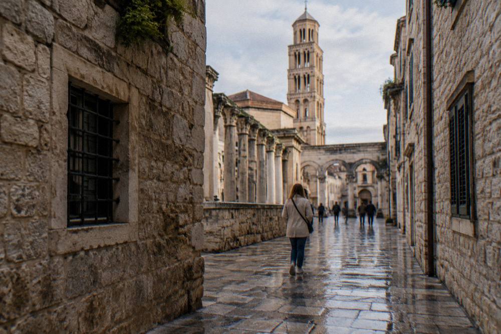 A visitor with a light jacket walking a wet stone street inside the old centre of Split
