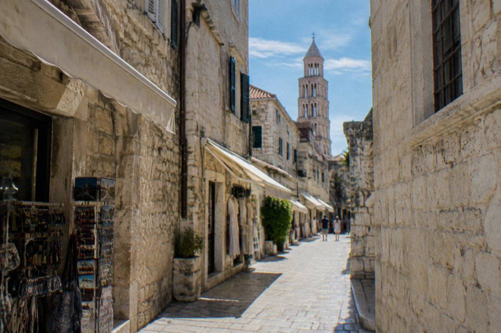 Sunlit limestone alley inside the old town of Split with white stone walls and shop awnings