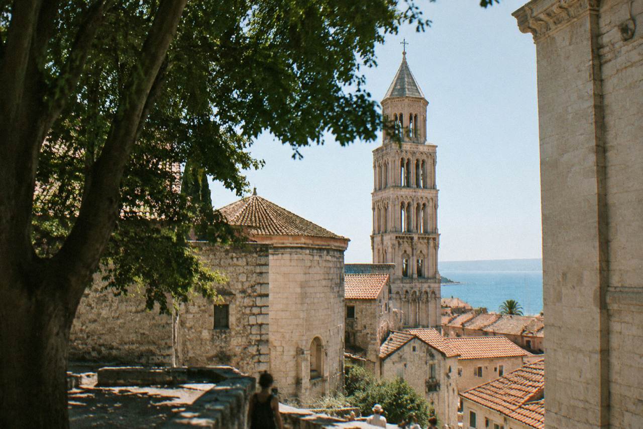 Sunlit stone buildings and a bell tower above the rooftops of Split old town near the sea