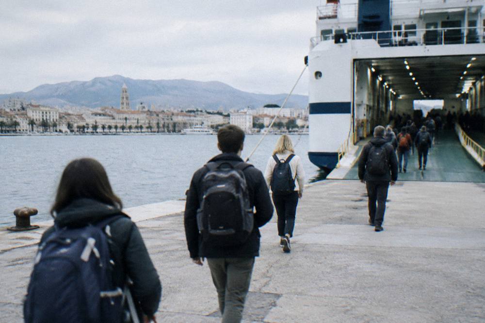 Travellers with backpacks walking toward a ferry ramp at Split port