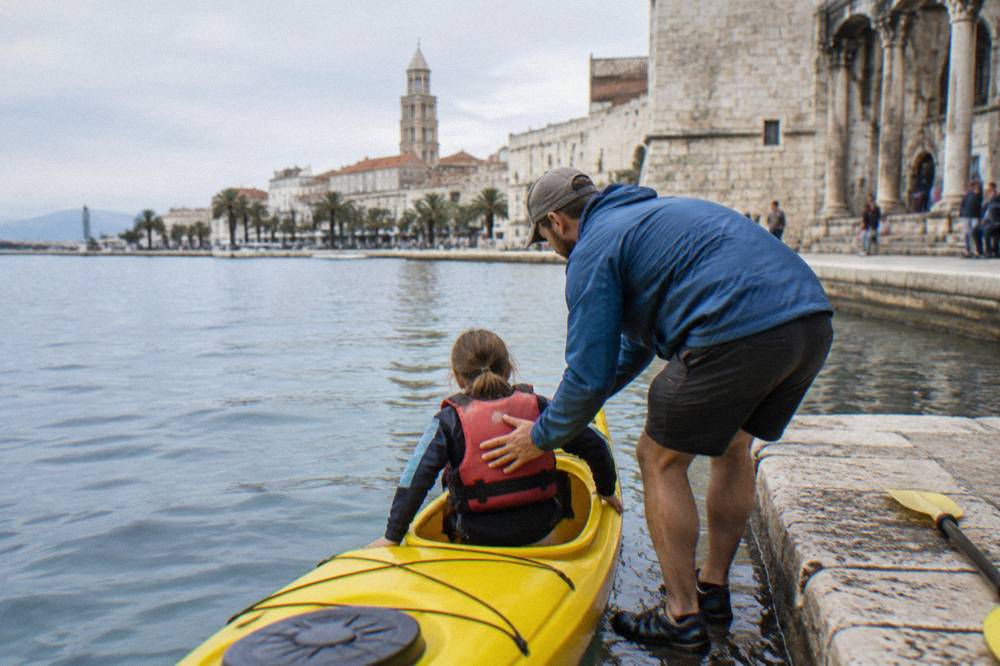 A guide helping a child into a kayak beside the sea in Split