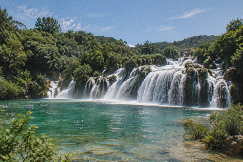 The wide travertine waterfalls of Krka National Park spilling into a green pool surrounded by forest