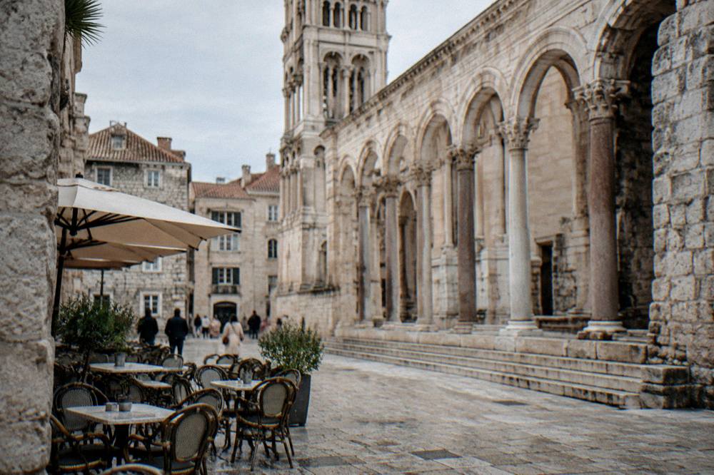 A stone square in Split Old Town with cafe tables and the facade of an ancient Roman building