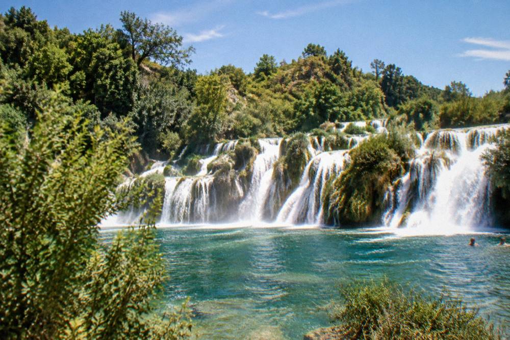 Waterfalls spilling over travertine barriers into a green pool at Krka National Park