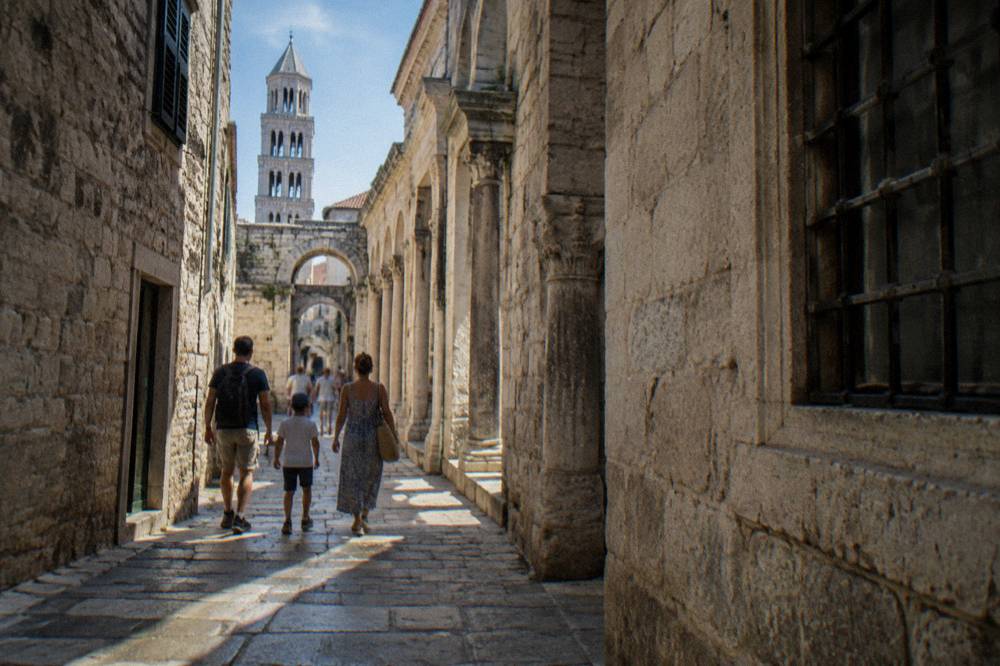 A family walking through a narrow stone alley inside the old town of Split